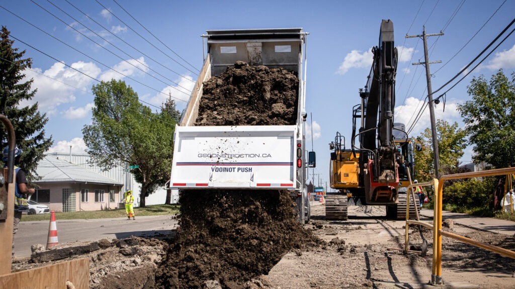 Dump truck unloading material into trench during watermain construction