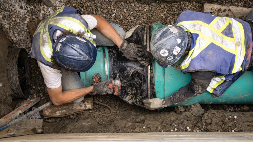 Two GS Construction workers securing and tying in underground pipes during sanitary and storm sewer installation